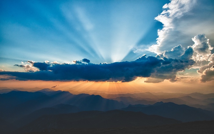 Sun rays shining through clouds over mountains