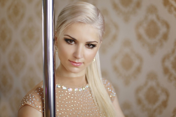 Blonde woman in a sparkly outfit posing by a pole