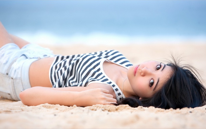 Asian woman with brunette hair lying on the beach