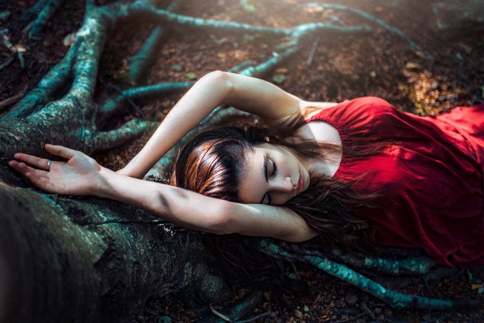 Woman in red dress lying down by tree roots