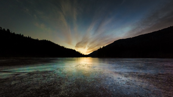 Sunset over a frozen lake between silhouetted mountains