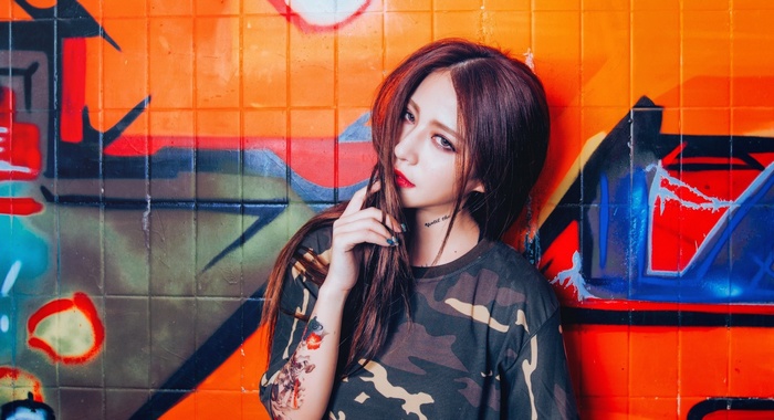 Asian woman with tattoos in front of graffiti wall