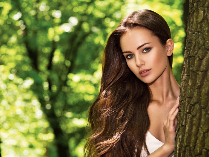 Woman with long brown hair peeking from behind a tree