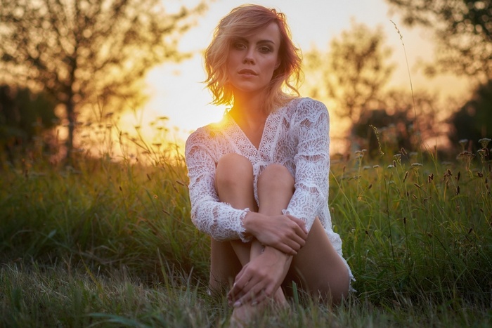 Woman in white lace dress sitting in a field at sunset