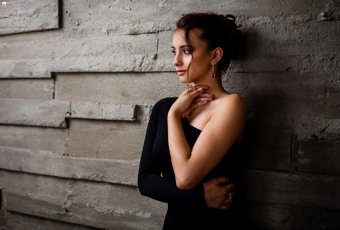 Woman in black dress leaning against a concrete wall