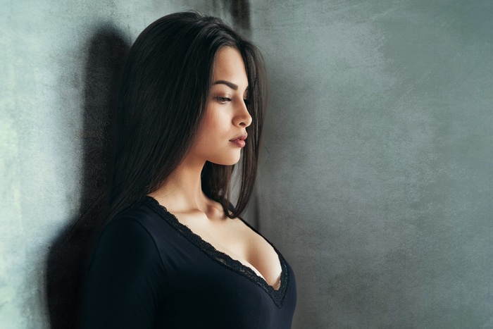 Woman with black hair leaning against a wall