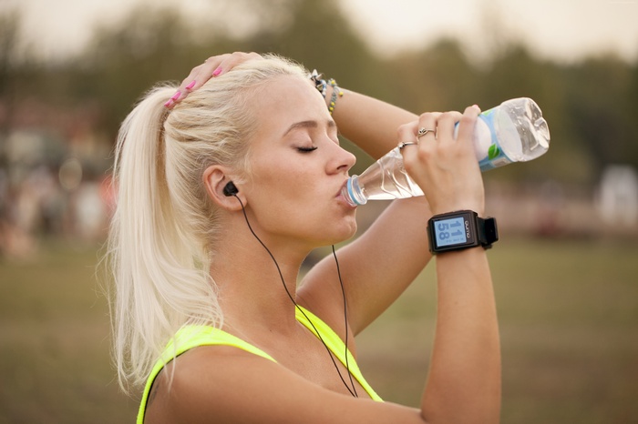 Woman in yellow clothing drinking water with QUMO watch