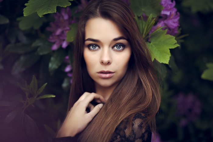 Woman with blue eyes and brown hair in front of purple flowers