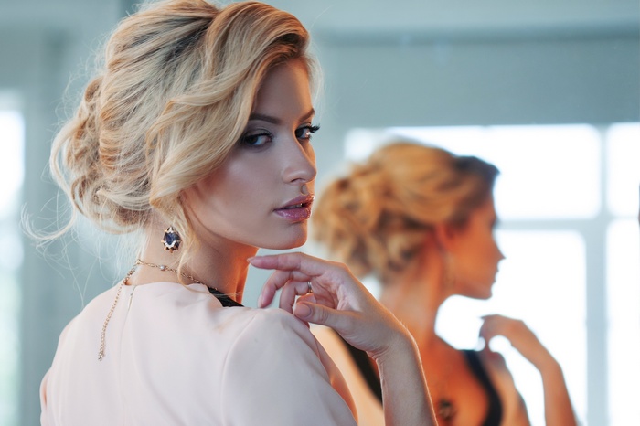 Woman with blonde hair in a bun looking in a mirror