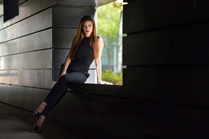 Woman in black jumpsuit sitting on ledge outdoors