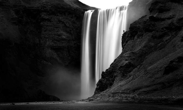 Monochrome waterfall with a lone figure on a cliff