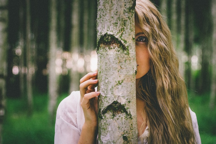 Woman peeking from behind a tree in a forest