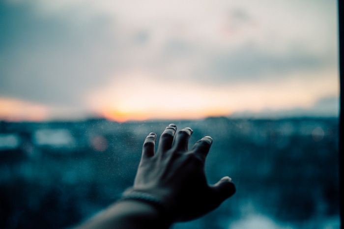 Hand reaching out towards a sunset over a city