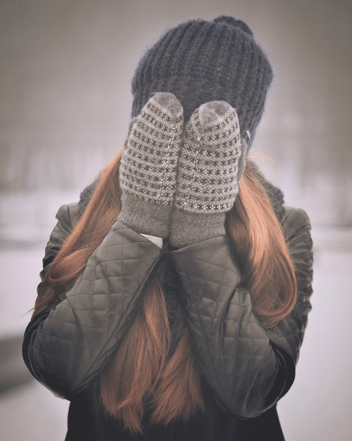 Woman in winter hat and mittens covering face