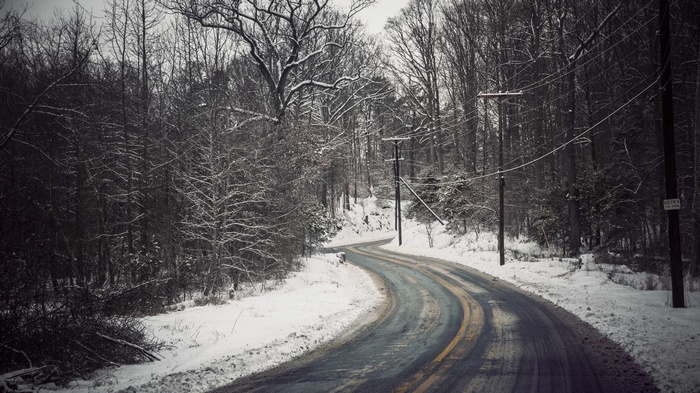 Winding snowy road through a winter forest with power lines
