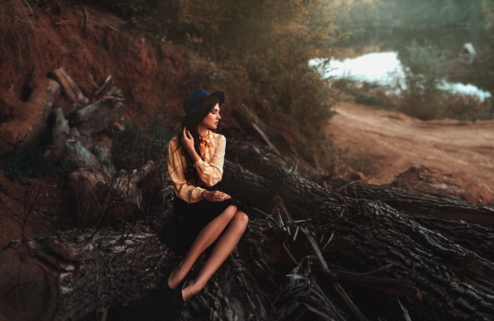 Woman in hat sitting on logs near water