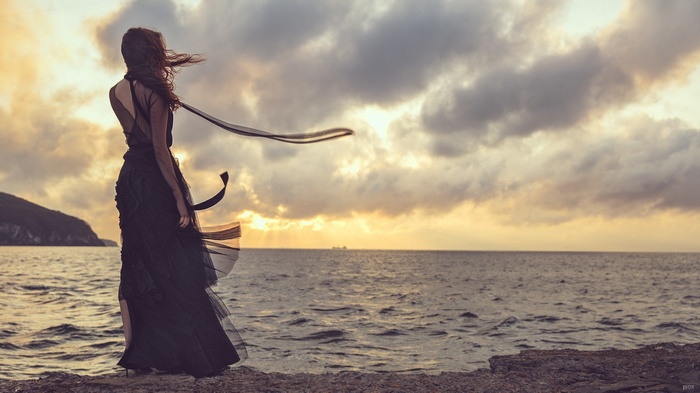 Woman in black dress by the sea at sunset