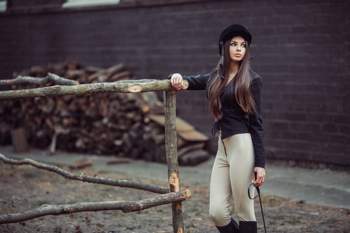 Woman in jockey attire with whip near wooden fence