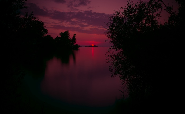 Sunset over a calm lake with silhouetted trees