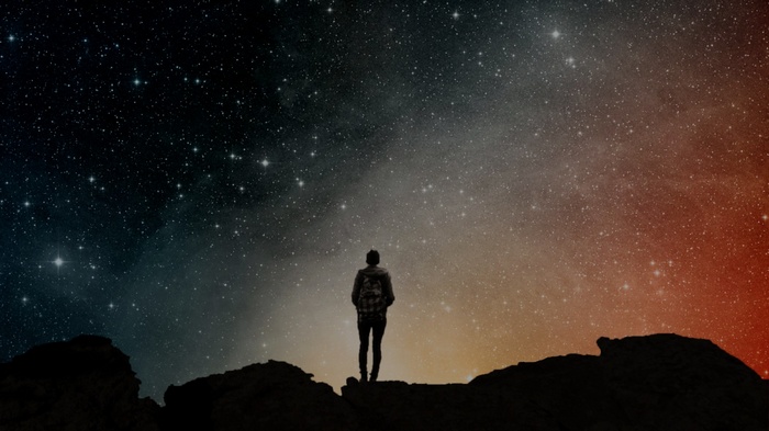 Person standing on rocks looking at starry sky