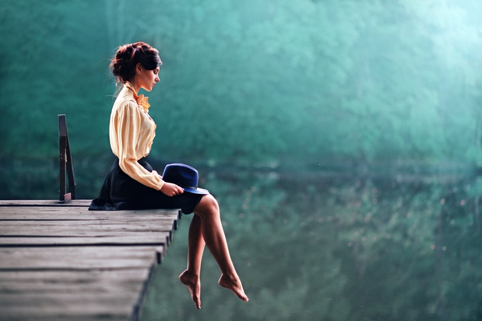 Woman with auburn hair sitting on a dock holding a hat