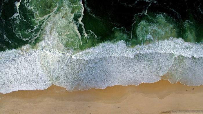 Aerial view of ocean waves crashing on a sandy beach