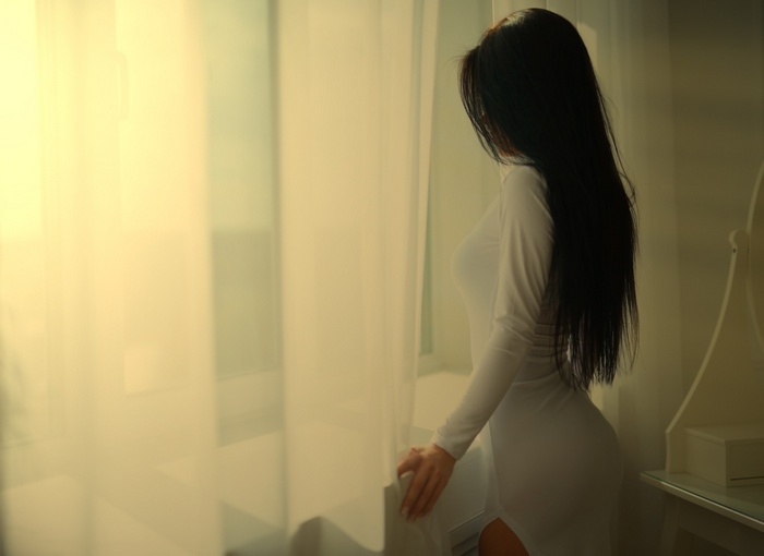 Woman with long black hair in a white dress by the window