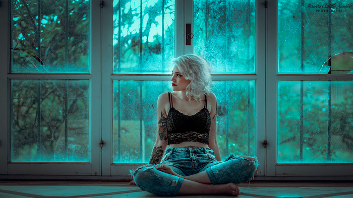 Woman with platinum blonde hair and tattoos sitting by a window