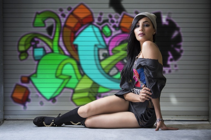 Woman with black hair sitting in front of graffiti