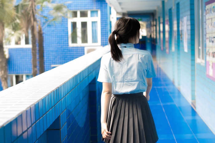 Asian girl in JK uniform walking down a school hallway