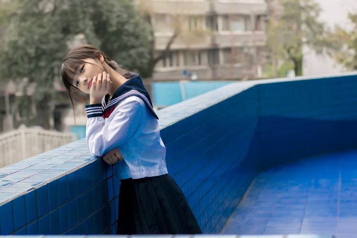 Asian girl in JK uniform leaning on a blue wall