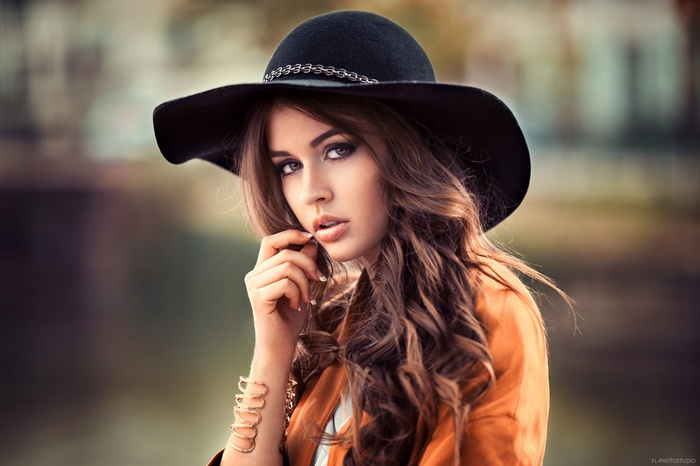 Woman with curly hair wearing a black hat and orange jacket