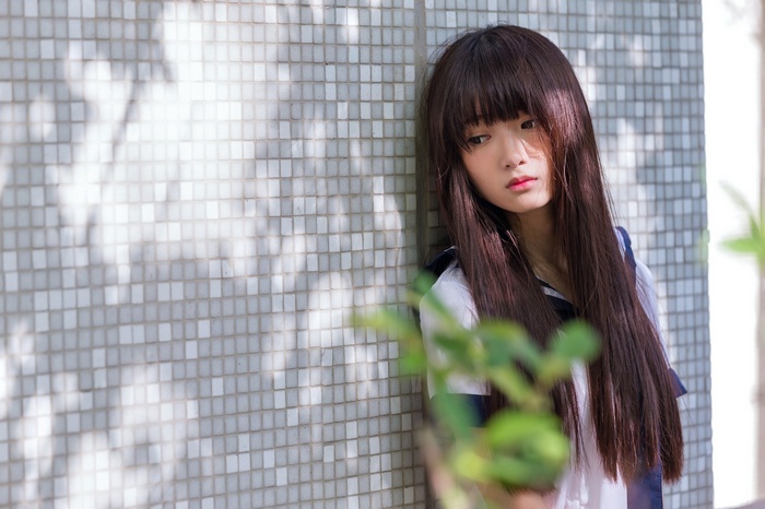 Asian woman with long hair leaning against a tiled wall