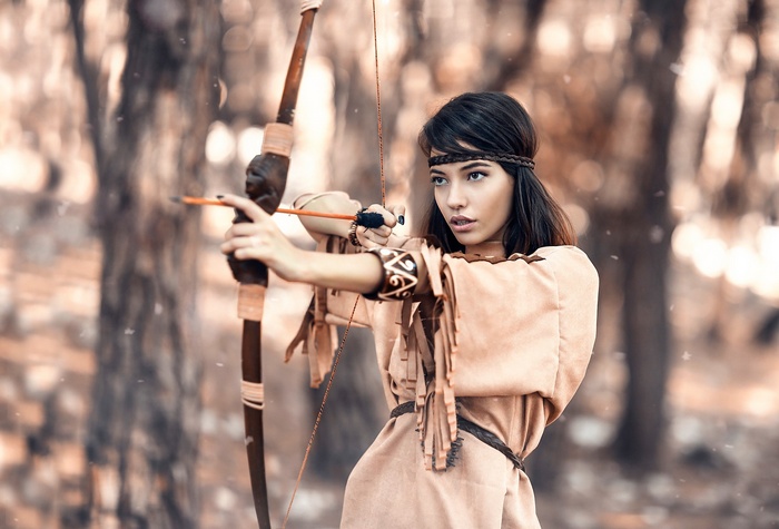 Woman in Native American attire aiming a bow and arrow