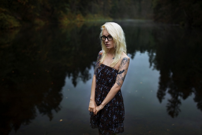 Woman with tattoos and glasses by a lake