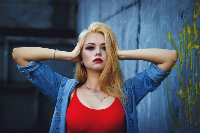 Woman with blonde hair and red top, hands on head