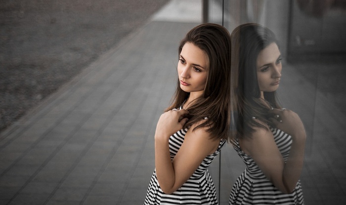 Woman in striped dress leaning against glass with reflection