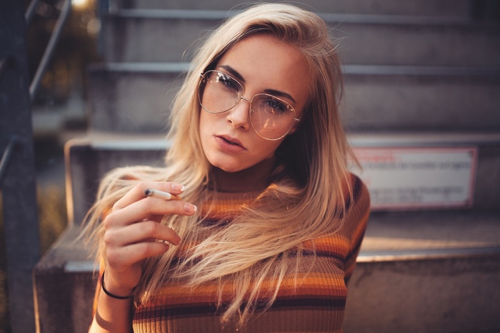 Woman with blonde hair and glasses smoking a cigarette