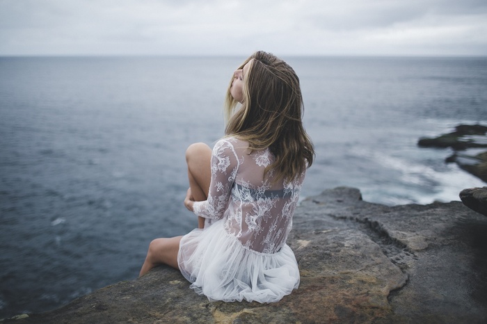 Woman in white dress sitting on a cliff by the sea