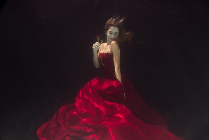 Woman in red dress holding a rose underwater