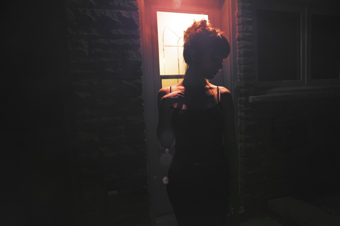 Woman in black tank top standing by a door at night