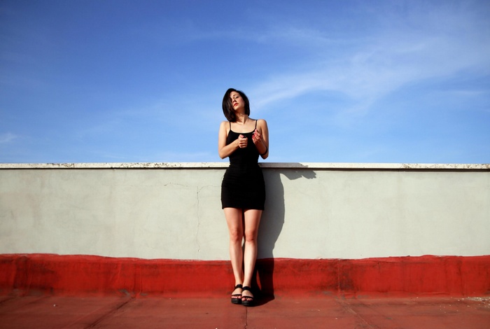 Woman in black dress on rooftop under blue sky