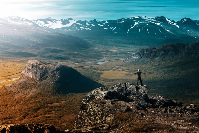 Person standing on a rocky outcrop overlooking a vast mountain valley
