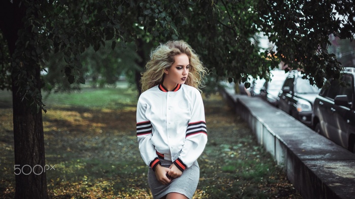 Woman with blonde hair in a bomber jacket and skirt