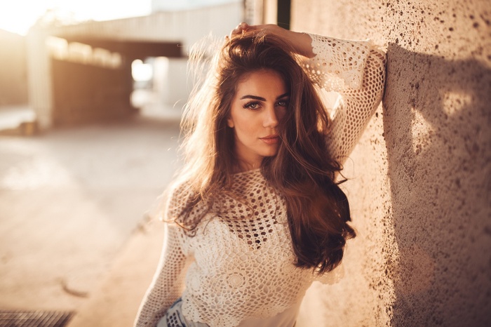 Woman with hands on head leaning against a wall at sunset