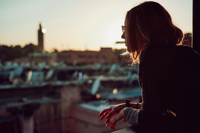 Woman smoking on a balcony overlooking a city at sunset