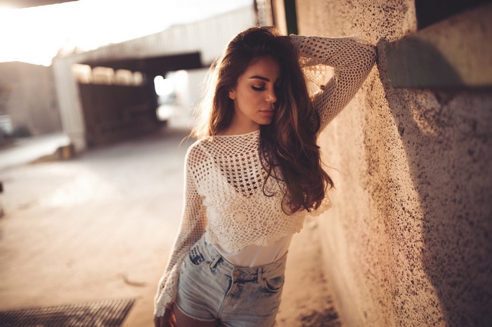 Woman in crochet top and jean shorts leaning against wall