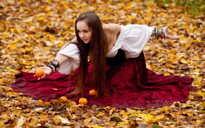 Woman in a red dress holding oranges in autumn leaves