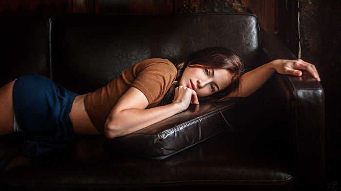 Woman lying on a leather couch by Georgy Chernyadyev