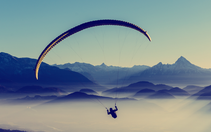 Paraglider soaring over misty mountains